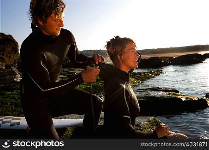Man helping woman with wetsuit