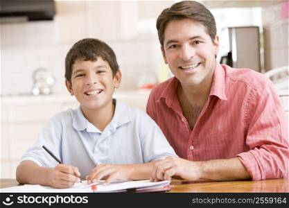 Man helping young boy in kitchen doing homework and smiling