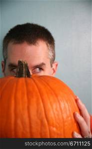 Man hiding behind a pumpkin