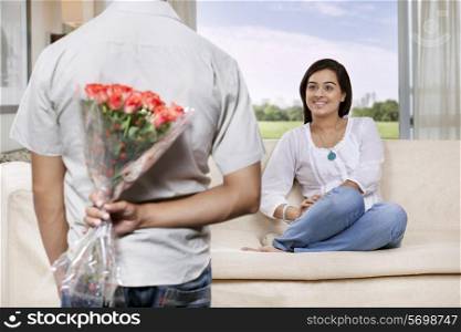 Man hiding bunch of flowers behind back while woman watching