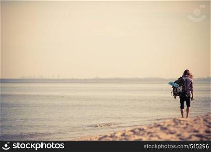 Man hiker backpacker walking with backpack on sea shore at sunny day. Adventure, summer, tourism active lifestyle. Young long haired guy tramping. Man hiker with backpack tramping by seaside