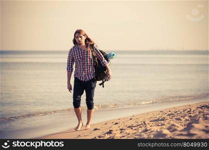 Man hiker backpacker walking with backpack on sea shore at sunny day. Adventure, summer, tourism active lifestyle. Young long haired guy tramping
