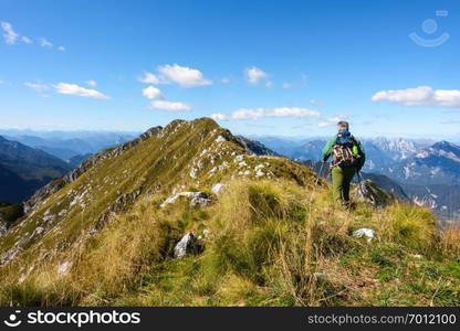 Man hiker walking on top of mountain against blue sky.