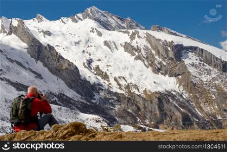 man hiker with camera and backpack taking picture of beautiful mountain