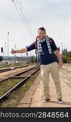Man hitchhiking on railroad train station smiling backpack travel tourist