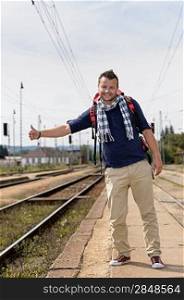 Man hitchhiking on railroad train station smiling backpack travel tourist