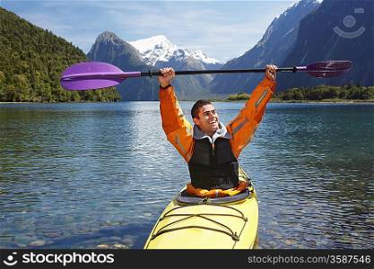 Man hoisting oar of kayak over head in mountain lake