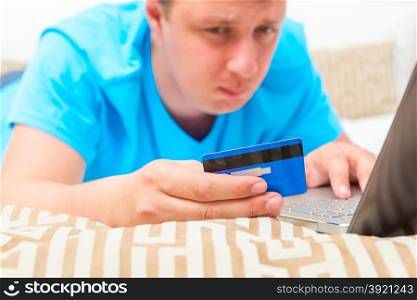 man holding a blue bank card lying on the bed