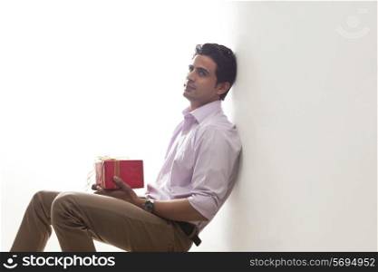 Man holding a gift leaning against wall