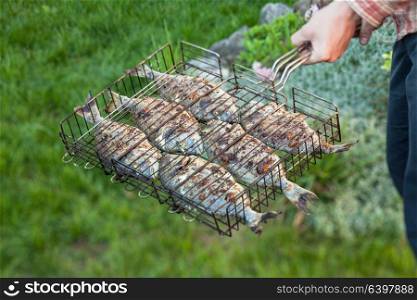 Man holding a grilled fish in a steel grid. Fish on the grill