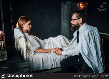 Man holding a hand of sick loved woman in hospital bed. Illness of female patient in clinic room, health recovery and treatment. Man holding a hand of sick loved woman in bed