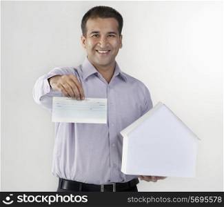 Man holding a house model and cheque