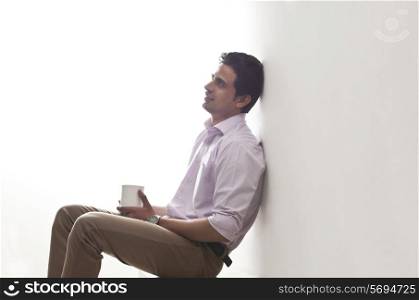 Man holding a mug of tea leaning against wall