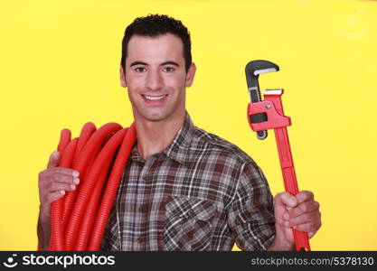 Man holding a pipe wrench and carrying corrugated tubing around his shoulder