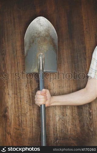Man holding a spade in front of wooden background.