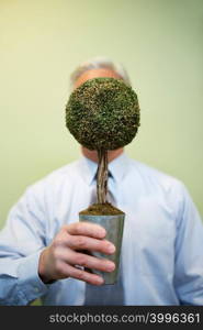 Man holding bonsai tree in front of his face