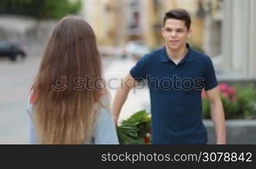 Man holding bouquet of flowers behind his back and surprising his cute girlfriend outdoors. Surprised young woman receiving flowers from attentive boyfriend and kissing him with love during romantic date.