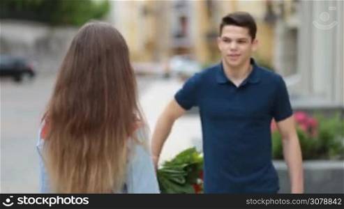 Man holding bouquet of flowers behind his back and surprising his cute girlfriend outdoors. Surprised young woman receiving flowers from attentive boyfriend and kissing him with love during romantic date.