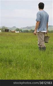 Man holding bucket in field, rear view