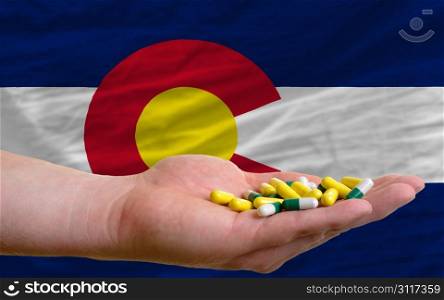 man holding capsules in front of complete wavy american state flag of colorado symbolizing health, medicine, cure, vitamines and healthy life