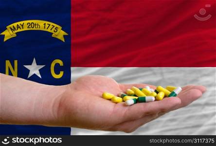 man holding capsules in front of complete wavy american state flag of north carolina symbolizing health, medicine, cure, vitamines and healthy life