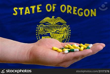 man holding capsules in front of complete wavy american state flag of oregon symbolizing health, medicine, cure, vitamines and healthy life