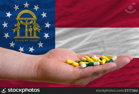 man holding capsules in front of complete wavy american state flag of georgia symbolizing health, medicine, cure, vitamines and healthy life