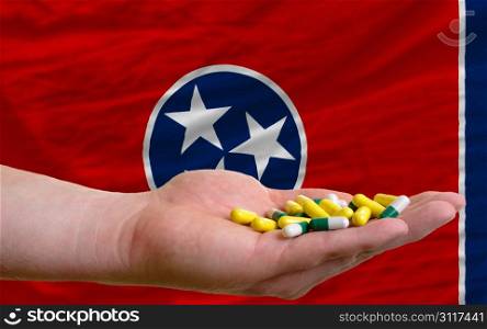 man holding capsules in front of complete wavy american state flag of tennessee symbolizing health, medicine, cure, vitamines and healthy life
