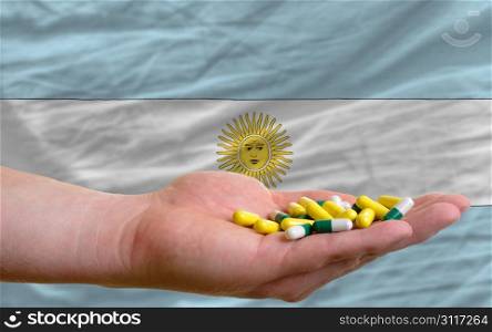 man holding capsules in front of complete wavy national flag of argentina symbolizing health, medicine, cure, vitamines and healthy life