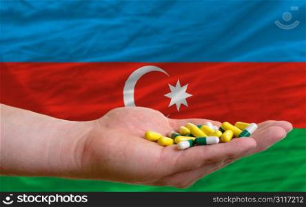 man holding capsules in front of complete wavy national flag of azerbaijan symbolizing health, medicine, cure, vitamines and healthy life