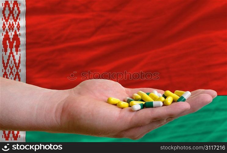 man holding capsules in front of complete wavy national flag of belarus symbolizing health, medicine, cure, vitamines and healthy life