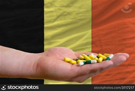 man holding capsules in front of complete wavy national flag of belgium symbolizing health, medicine, cure, vitamines and healthy life