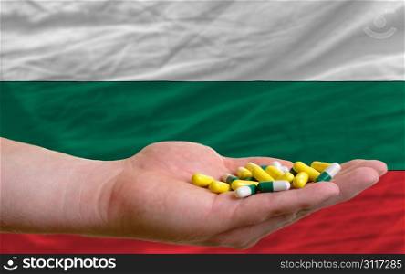 man holding capsules in front of complete wavy national flag of bulgaria symbolizing health, medicine, cure, vitamines and healthy life