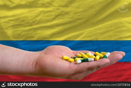 man holding capsules in front of complete wavy national flag of colombia symbolizing health, medicine, cure, vitamines and healthy life