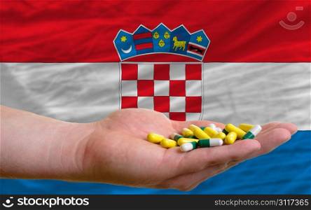 man holding capsules in front of complete wavy national flag of croatia symbolizing health, medicine, cure, vitamines and healthy life