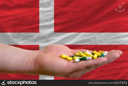man holding capsules in front of complete wavy national flag of denmark symbolizing health, medicine, cure, vitamines and healthy life