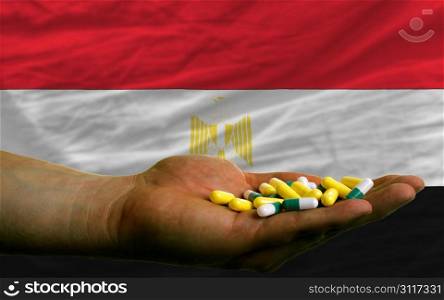 man holding capsules in front of complete wavy national flag of egypt symbolizing health, medicine, cure, vitamines and healthy life