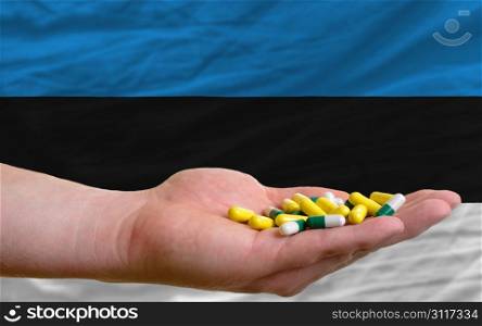 man holding capsules in front of complete wavy national flag of estonia symbolizing health, medicine, cure, vitamines and healthy life