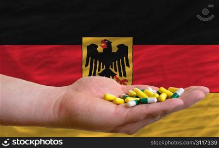 man holding capsules in front of complete wavy national flag of germany symbolizing health, medicine, cure, vitamines and healthy life
