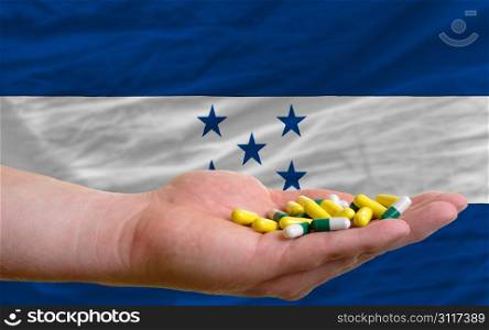 man holding capsules in front of complete wavy national flag of honduras symbolizing health, medicine, cure, vitamines and healthy life