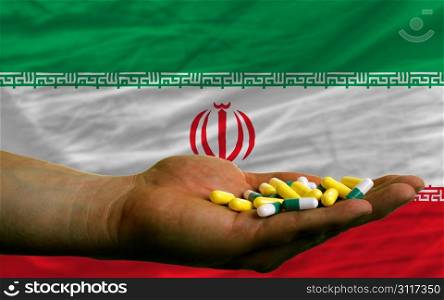 man holding capsules in front of complete wavy national flag of iran symbolizing health, medicine, cure, vitamines and healthy life