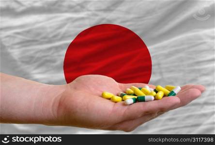 man holding capsules in front of complete wavy national flag of japan symbolizing health, medicine, cure, vitamines and healthy life