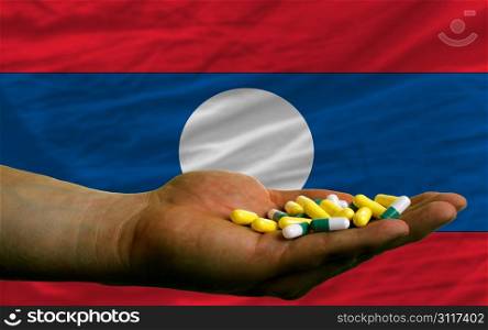 man holding capsules in front of complete wavy national flag of laos symbolizing health, medicine, cure, vitamines and healthy life