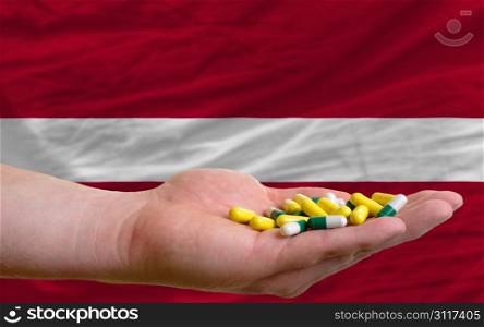 man holding capsules in front of complete wavy national flag of latvia symbolizing health, medicine, cure, vitamines and healthy life