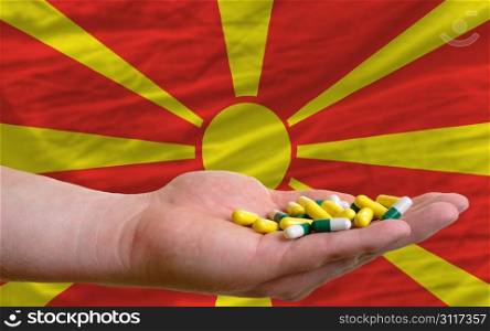 man holding capsules in front of complete wavy national flag of macedonia symbolizing health, medicine, cure, vitamines and healthy life