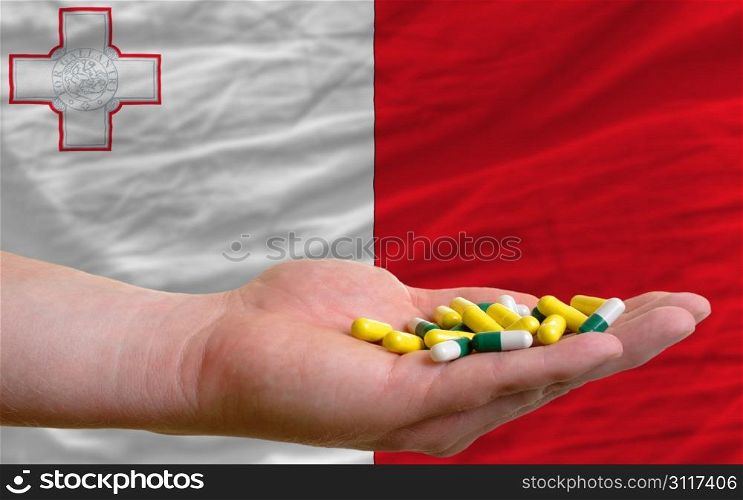 man holding capsules in front of complete wavy national flag of malta symbolizing health, medicine, cure, vitamines and healthy life
