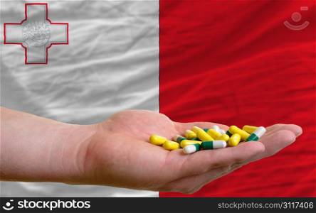 man holding capsules in front of complete wavy national flag of malta symbolizing health, medicine, cure, vitamines and healthy life