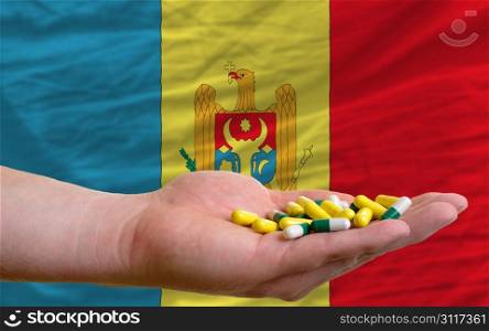 man holding capsules in front of complete wavy national flag of moldova symbolizing health, medicine, cure, vitamines and healthy life