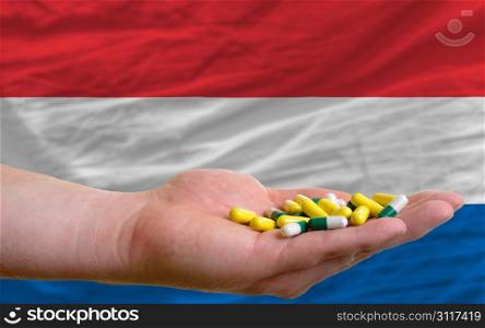 man holding capsules in front of complete wavy national flag of netherlands symbolizing health, medicine, cure, vitamines and healthy life
