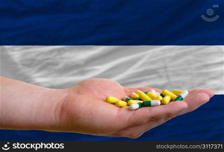 man holding capsules in front of complete wavy national flag of nicaragua symbolizing health, medicine, cure, vitamines and healthy life